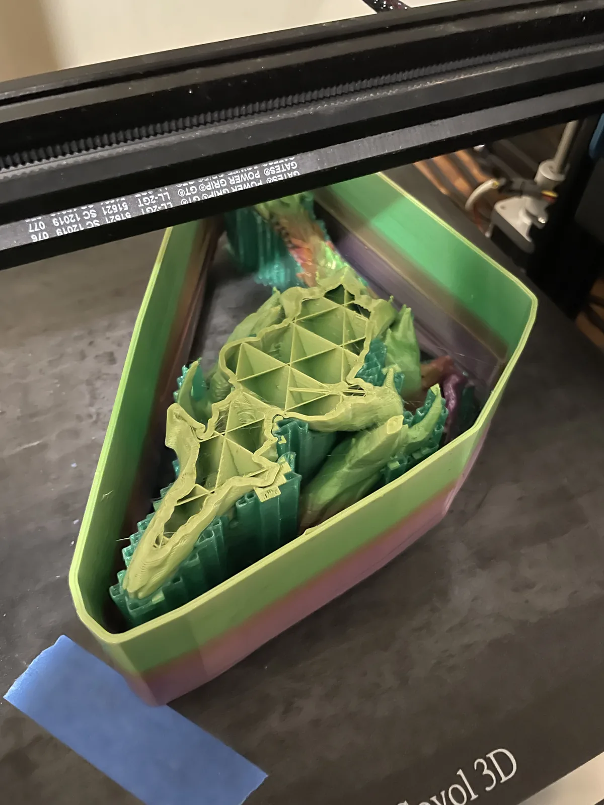 A green and yellow dragon-shaped print with lattice infill visible inside a green tray on a printer