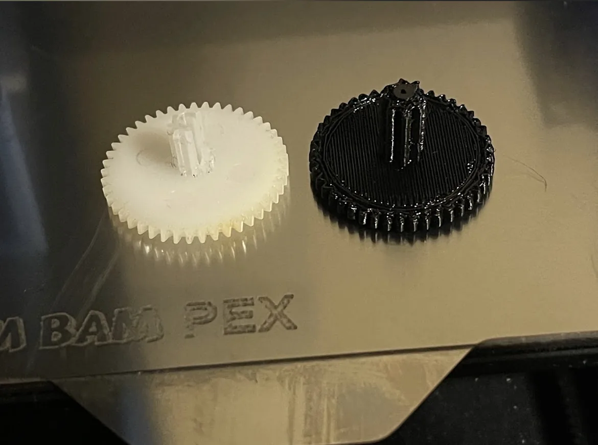 A white printed gear and a black printed gear on a textured metal print plate