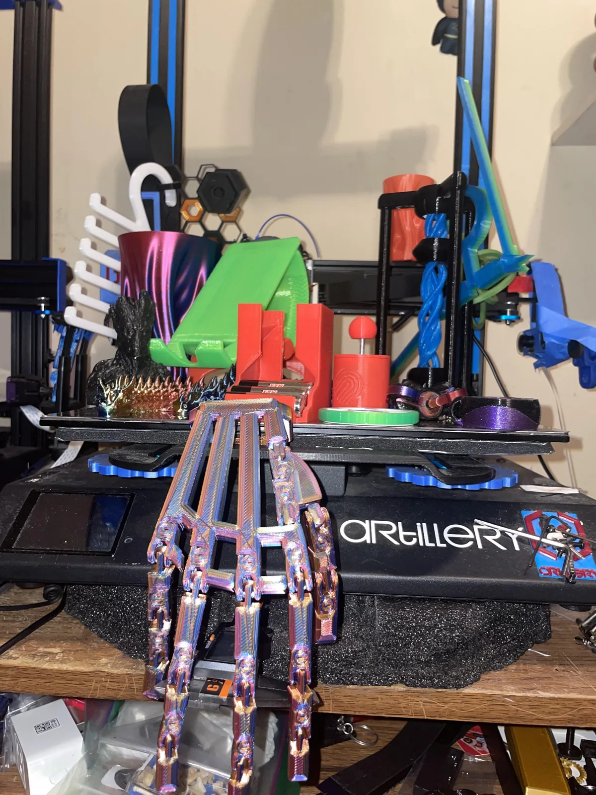Articulated multicolour hands hanging from a printer bed with other colourful prints behind