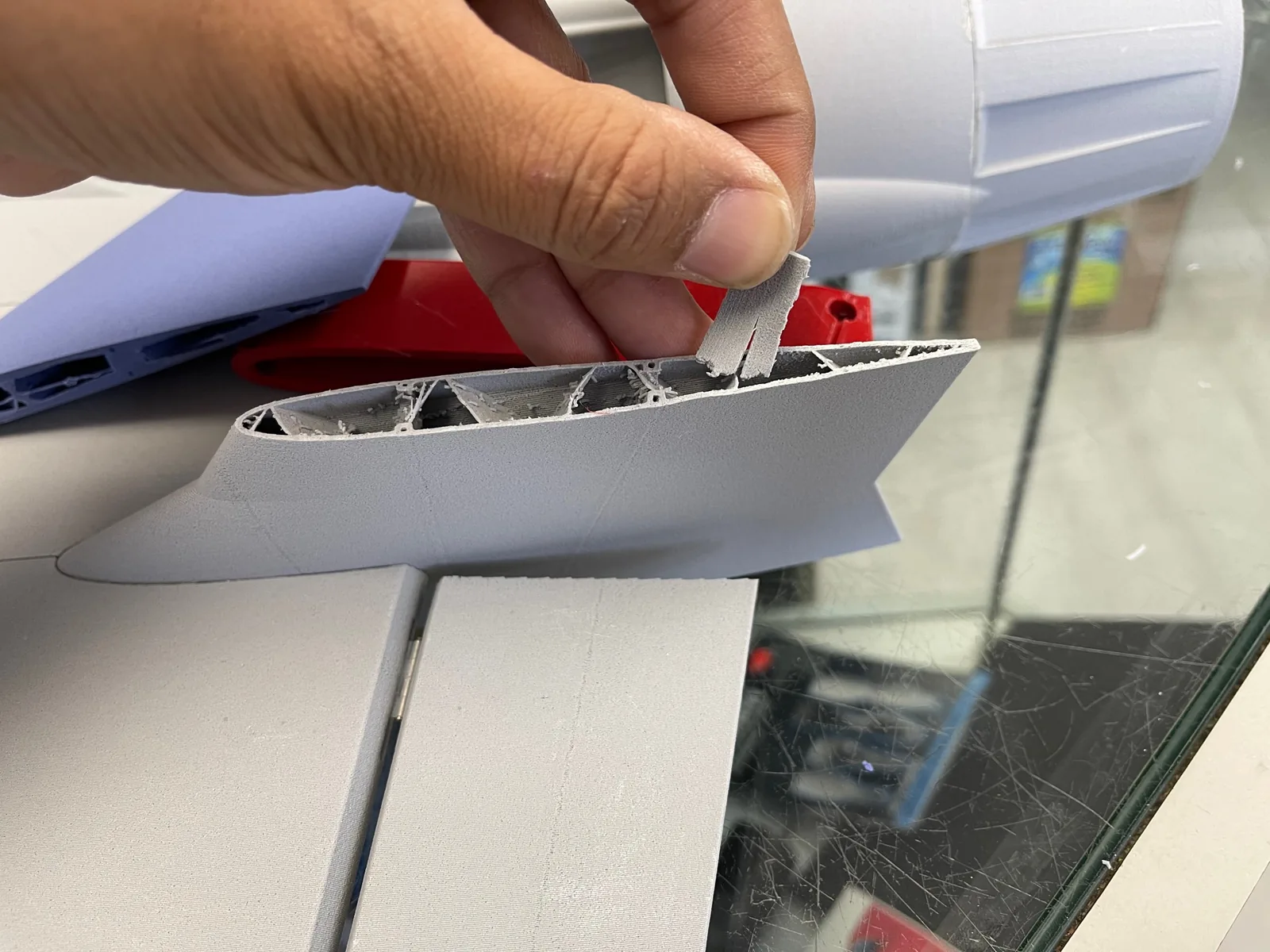 A hand holding a thin grey tab inside a cut-open printed fin showing internal ribs