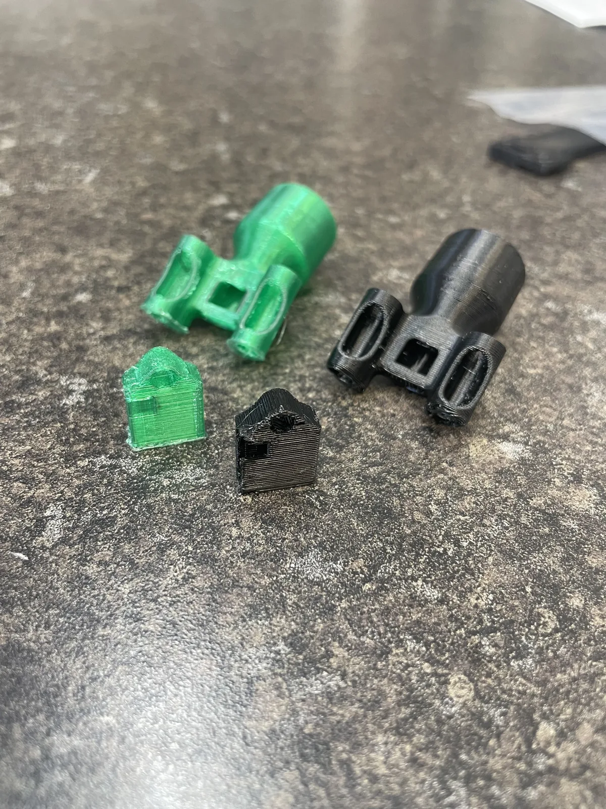 Four small printed parts, two green and two black, including clips and tube-shaped fittings